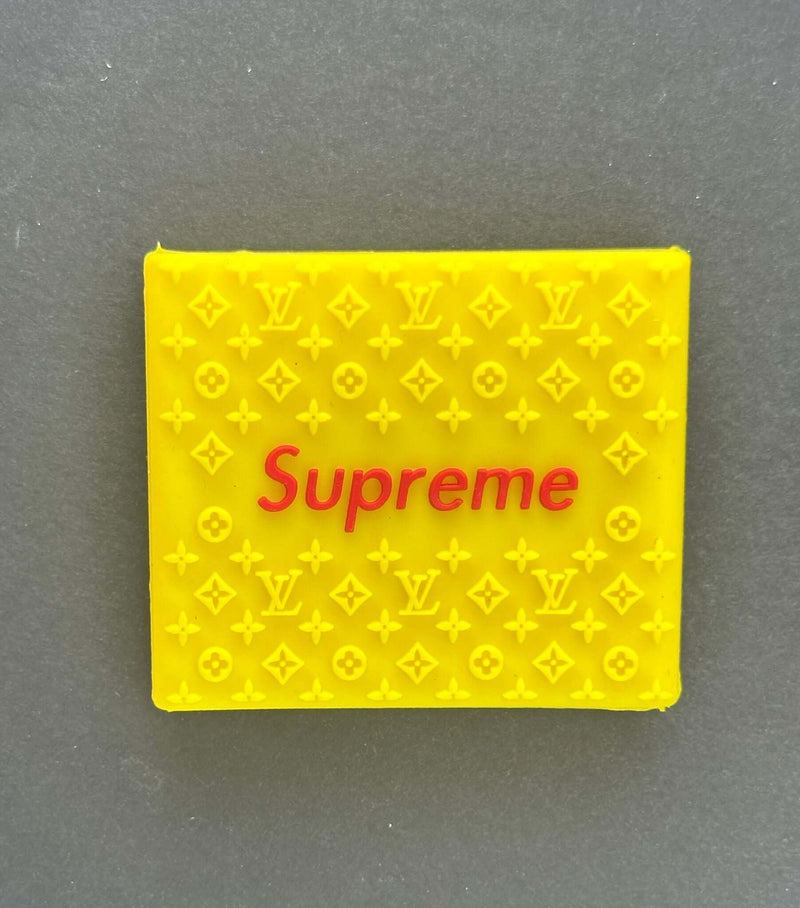 Bright yellow rubber grip featuring the word 'Supreme' in red, adorned with luxury brand patterns.