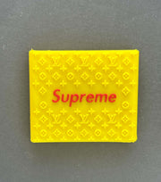 Bright yellow silicone grip displaying 'Supreme' logo with Louis Vuitton pattern background.